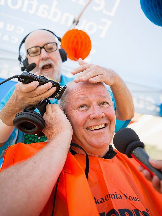 A man smiles as his head his shaved by another man in a tent