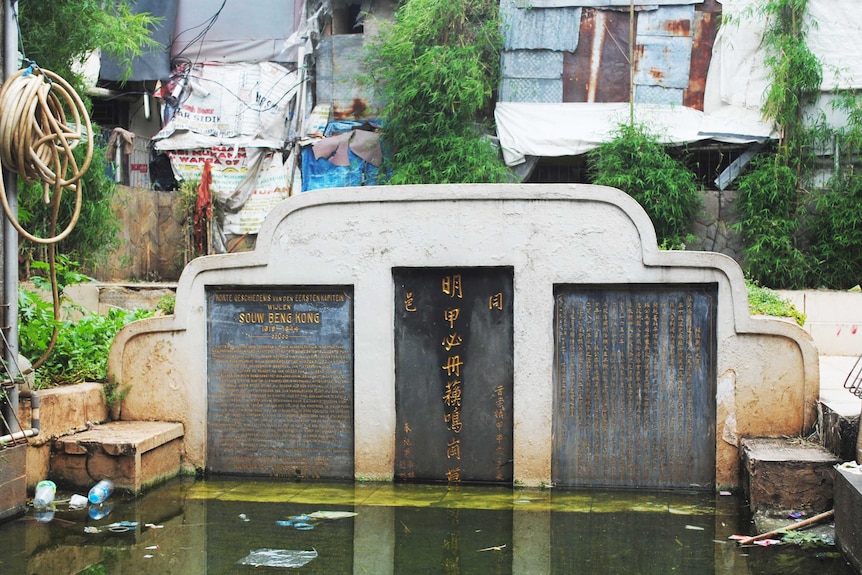 A large tomb, which takes up three panels of a wall, juts out from a pool of water.