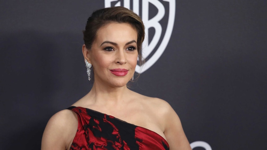 Alyssa Milano stands before the camera posing in a read dress.