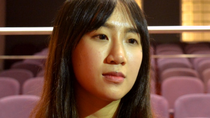 A woman looks past the camera as she stands in an empty auditorium with purple seats.