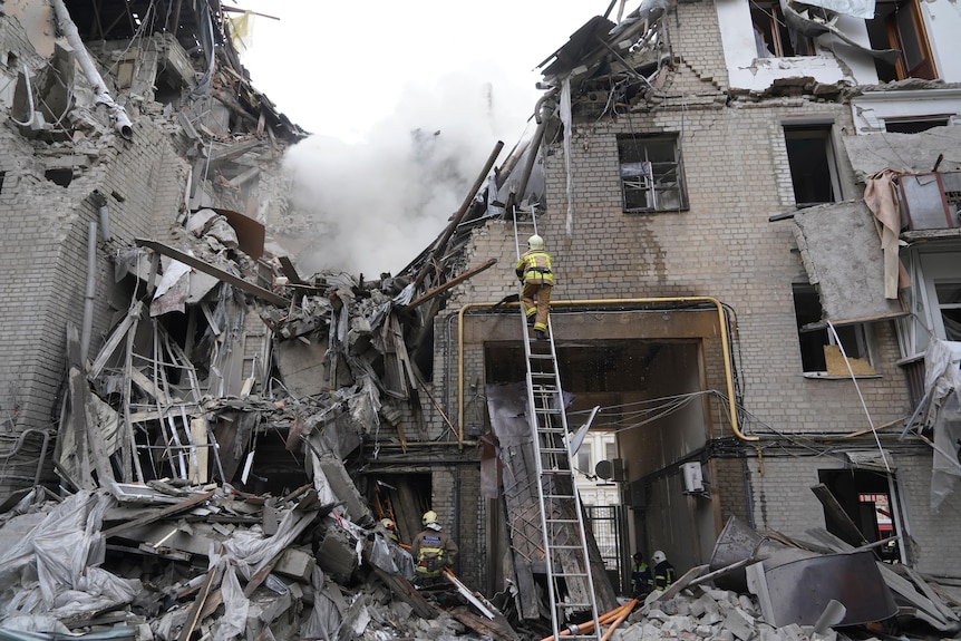 Ukrainian firefighters work in a destroyed building as smoke rises.