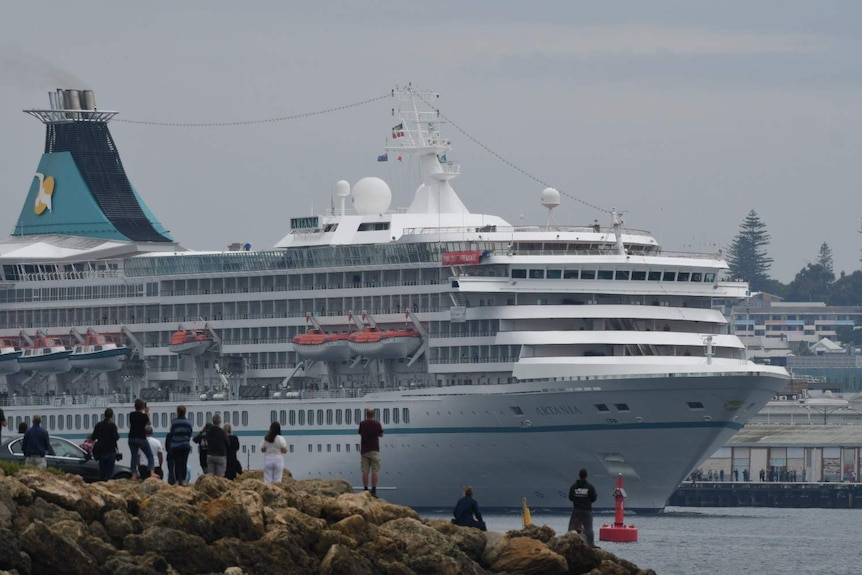 Cruise ship Artania sailing out of Fremantle Port watched by crowd of spectators on rocks