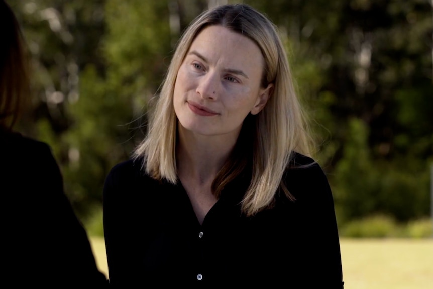 A blonde woman sits on a bench facing another woman, listening