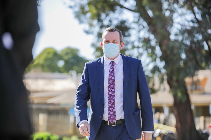 WA Premier Mark McGowan walks towards a press conference while wearing a suit and a face mask