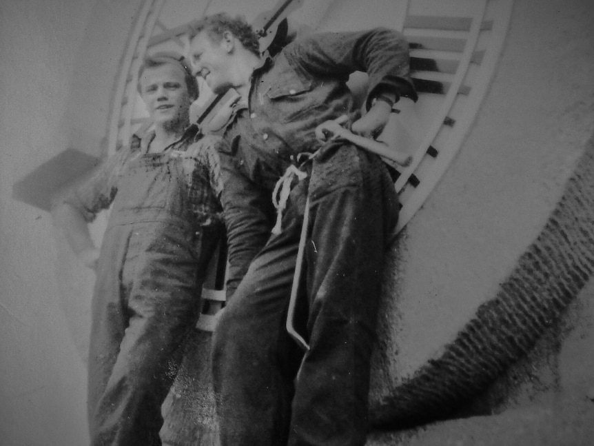 Scratchy monotone image of two workers with tools, standing in front of huge clock face.