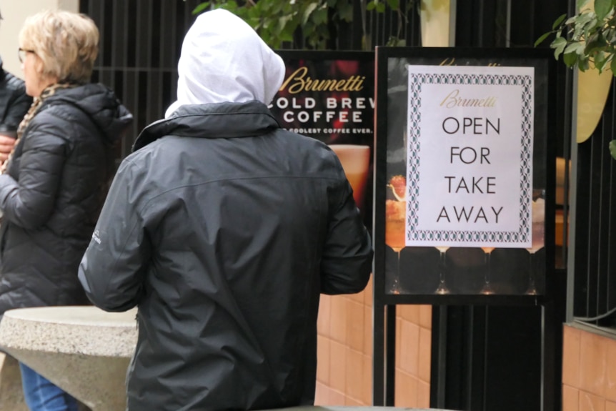 A man with his back to camera next to a takeaway coffee sign.