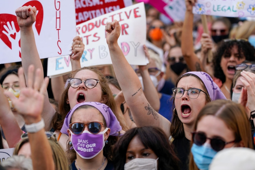 a crowd of woman wearing pro choice clothes and holding pro choice signs and raise their fists and shout