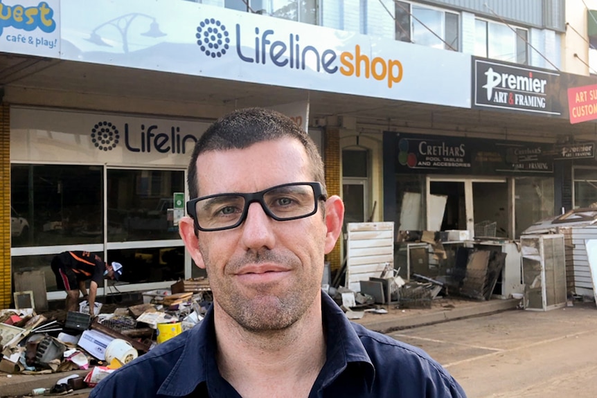 Michael Were stands in front of the destroyed Lismore Lifeline store, with flood debris in front of the shop.