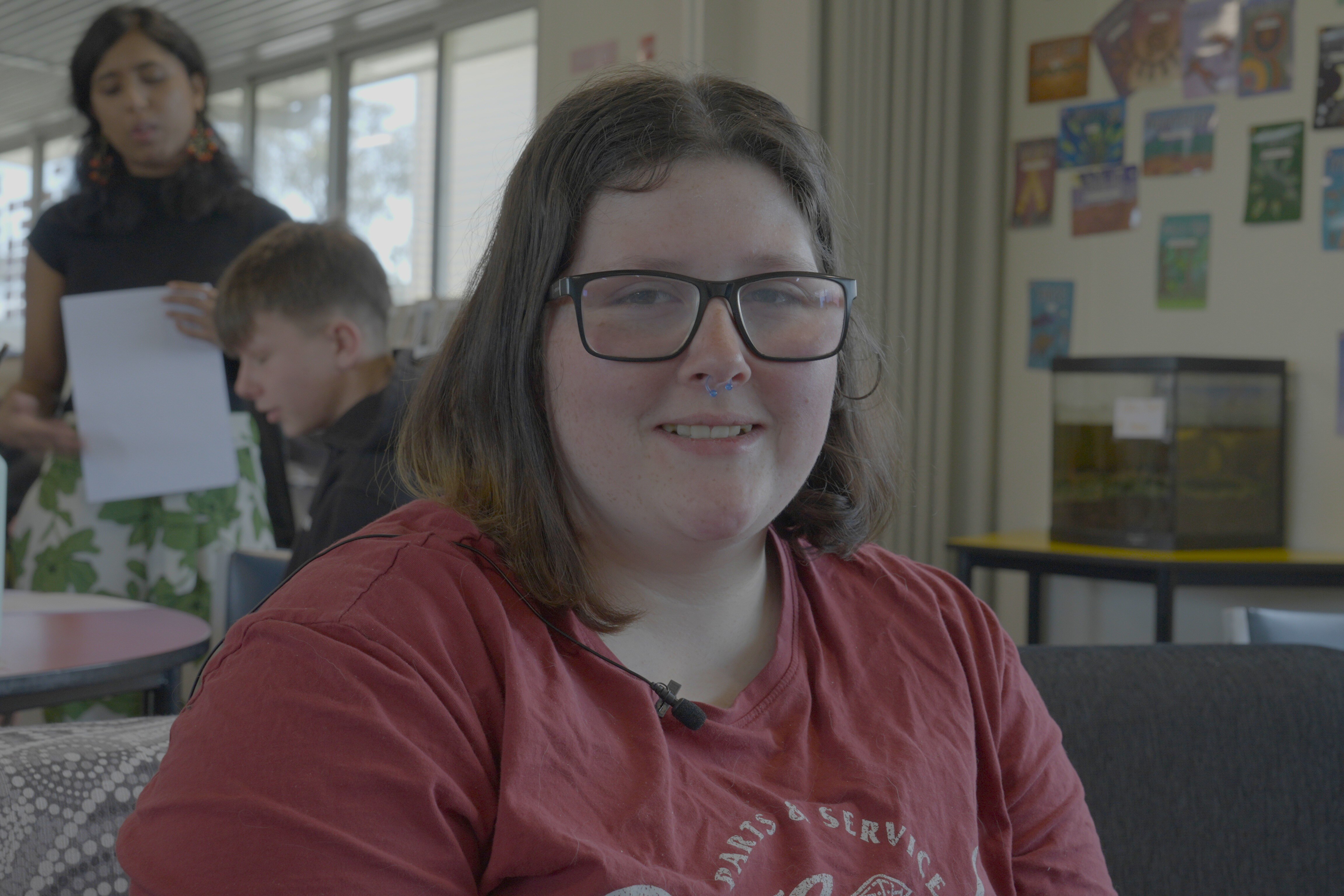 A young woman with shoulder length, straight hair smiles. She is wearing glasses.