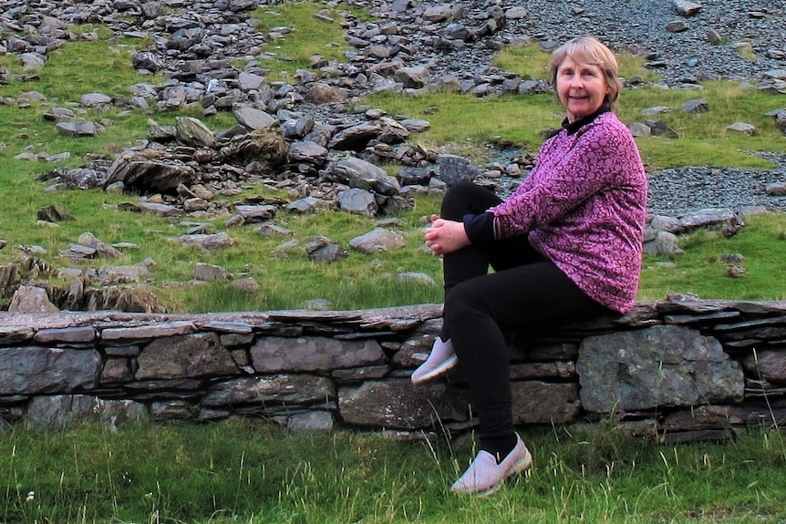 Woman sits on a rock wall among grass