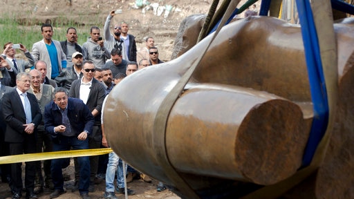 Onlookers watch as the torso of an ancient Egyptian pharaoh statue is excavated in a Cairo suburb.