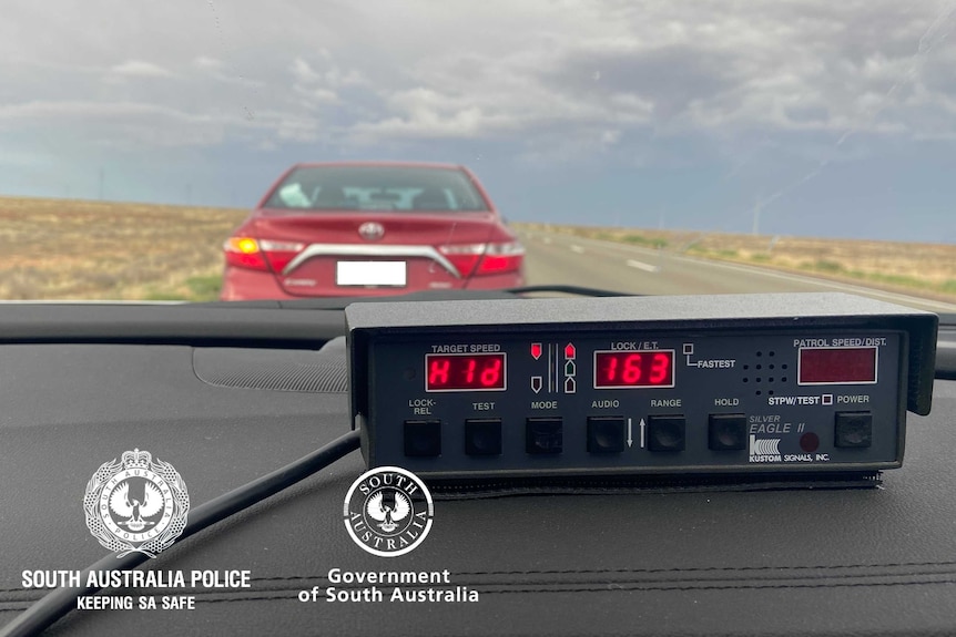 The dash of a police car showing the speed of a vehicle with a maroon Toyota Camry in the background.