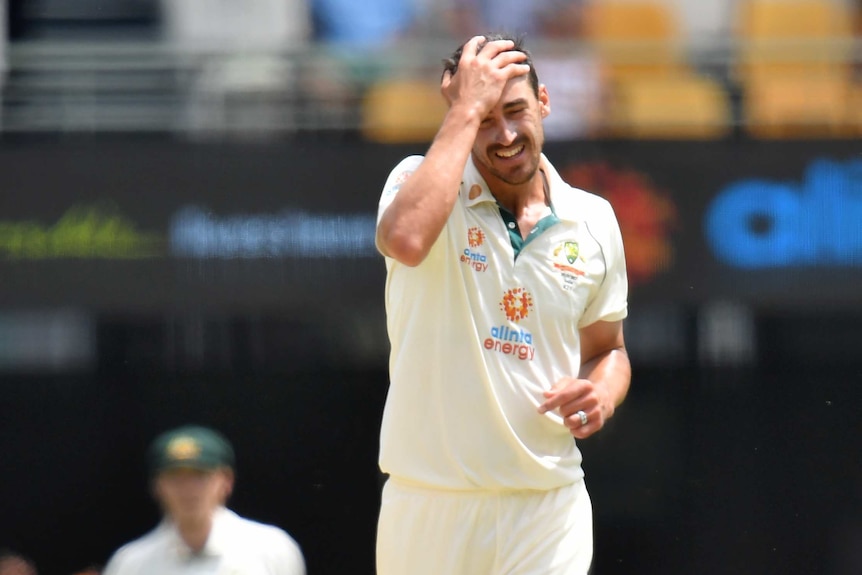 A male Australian fast bowler rubs his head with his right hand.