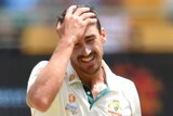 A male Australian fast bowler rubs his head with his right hand.