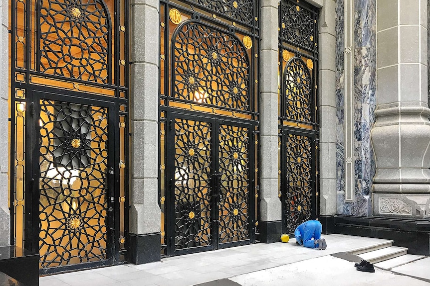 Construction worker prays outside the gates of a mosque
