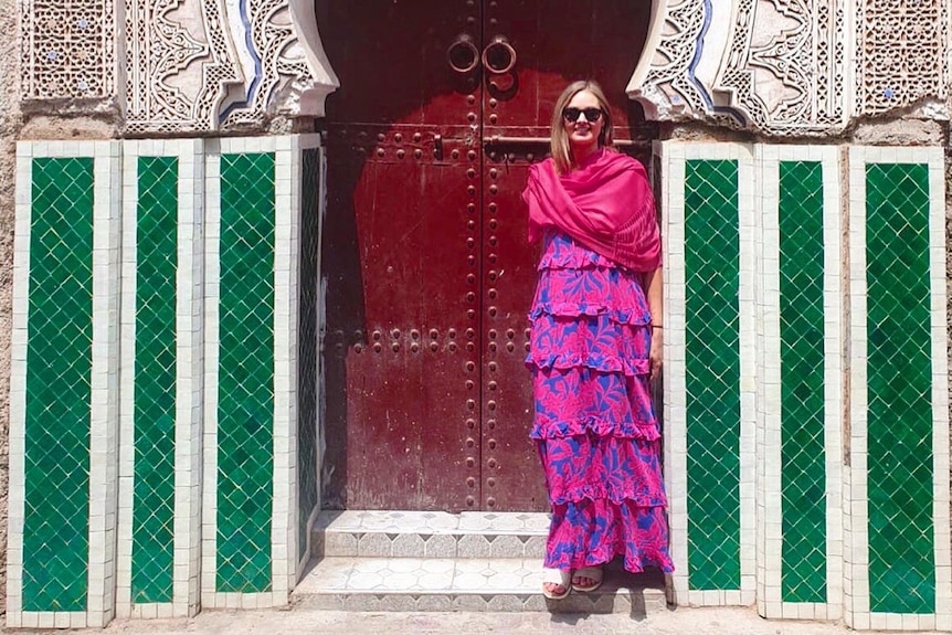 A woman wearing bright pink clothes standing in front of a green and white striped building with a red door.