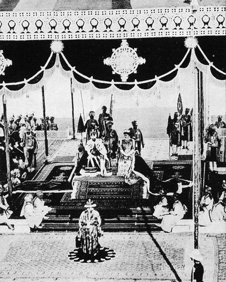 balck and white photo of two royals sit on a platform under a tent
