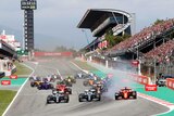 A group of Formula 1 cars race around a corner in front of large crowds.