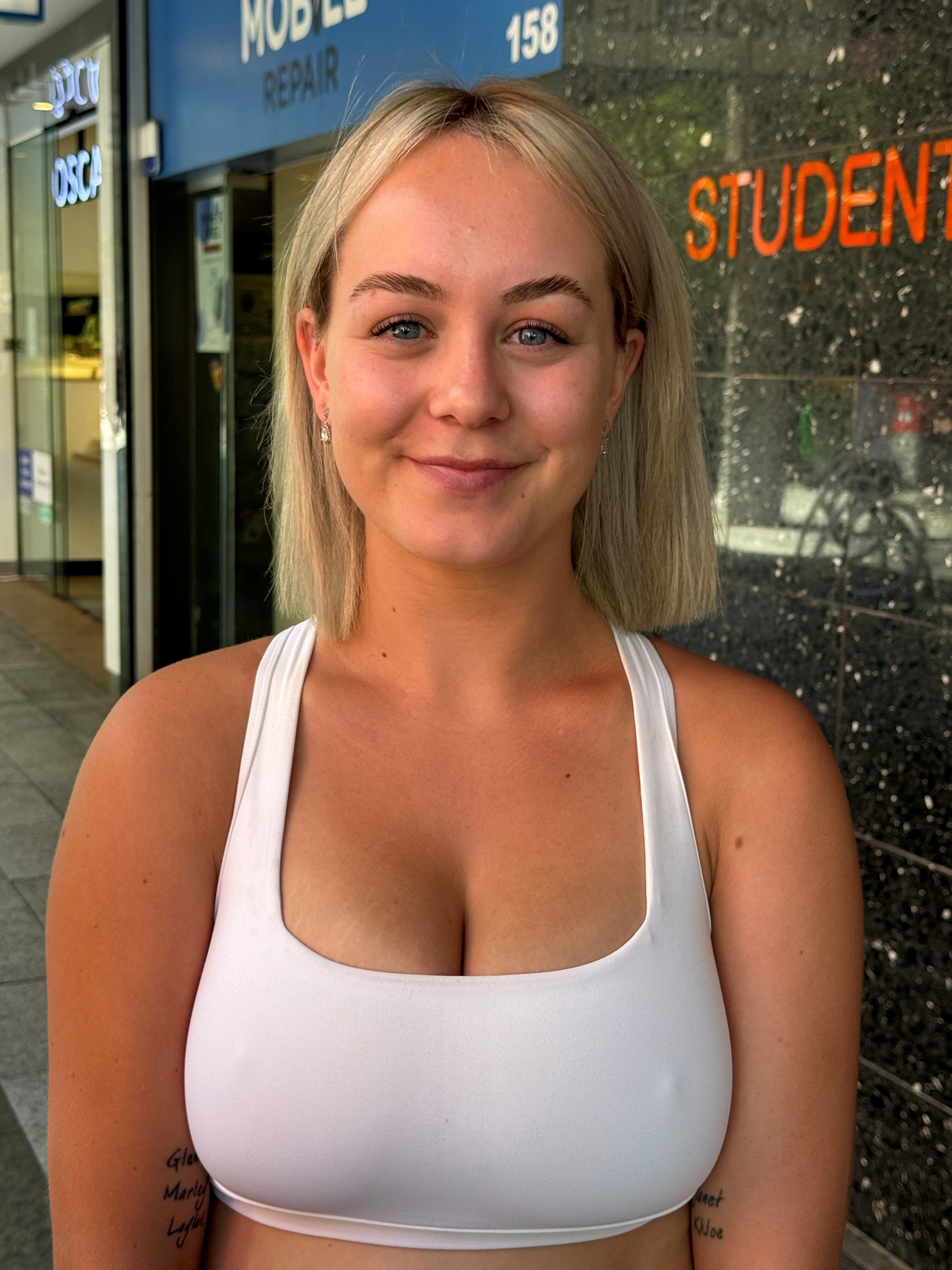 A woman in a white tank top smiling while standing in front of a shop