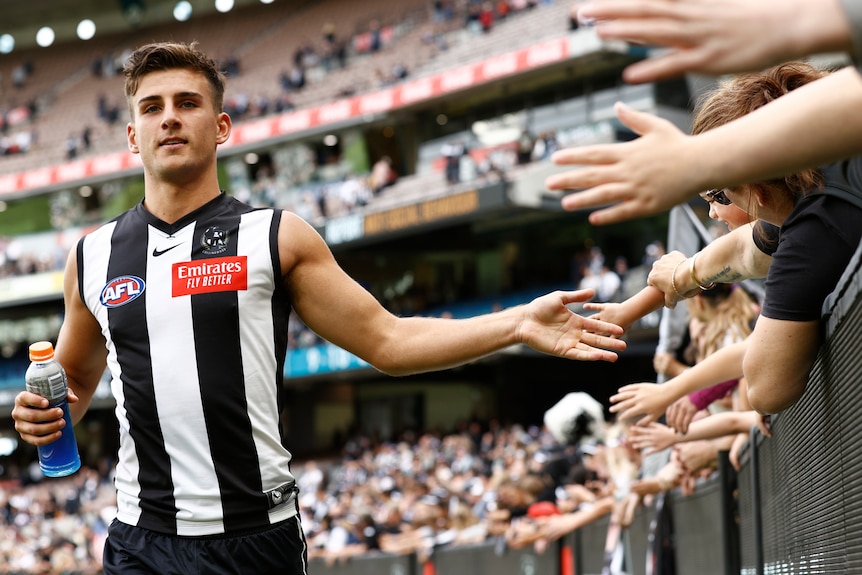 Nick Daicos runs along the fence line high-fiving members of the crowd