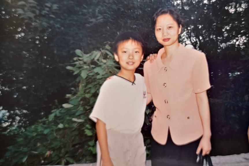 A photo of a boy in white shirt with his hand on his mother's shoulder. She is in a peach blazer. 
