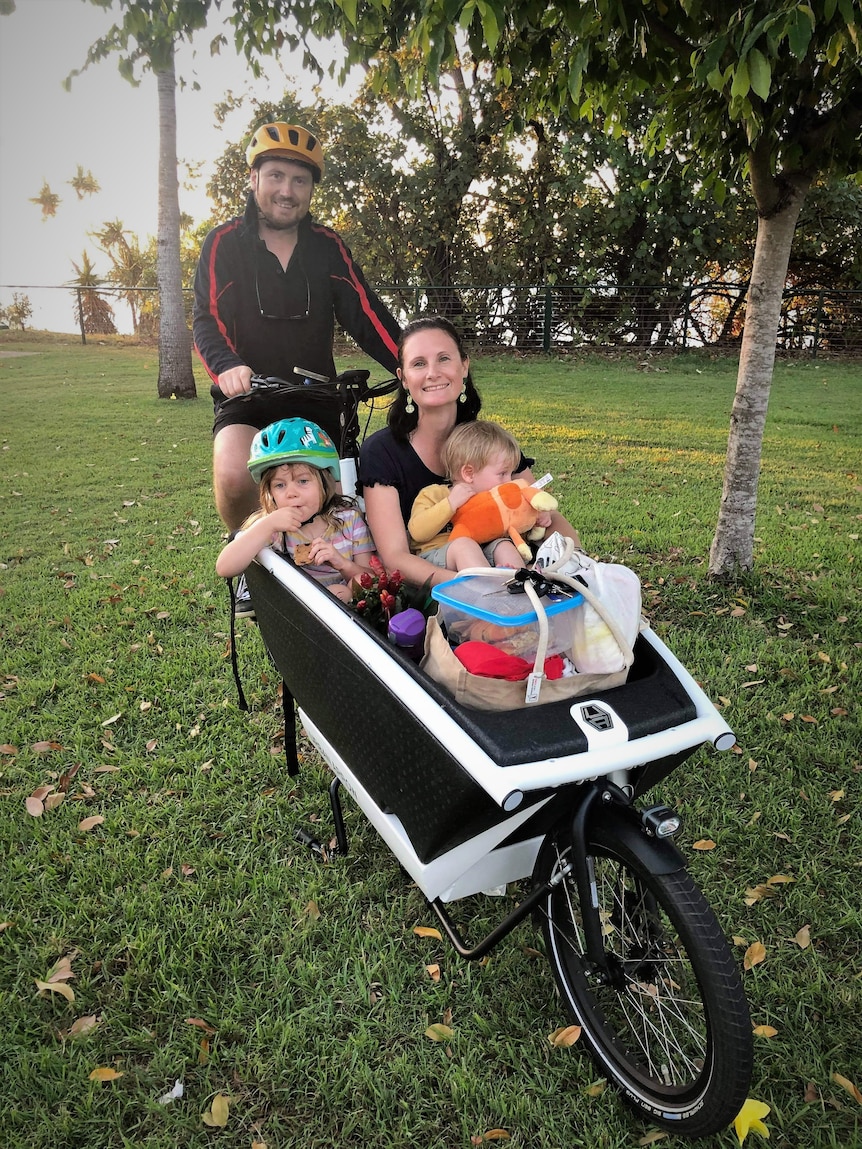 Dad on the saddle with mum, two kids, and loads of stuff in the box of a cargo bike.