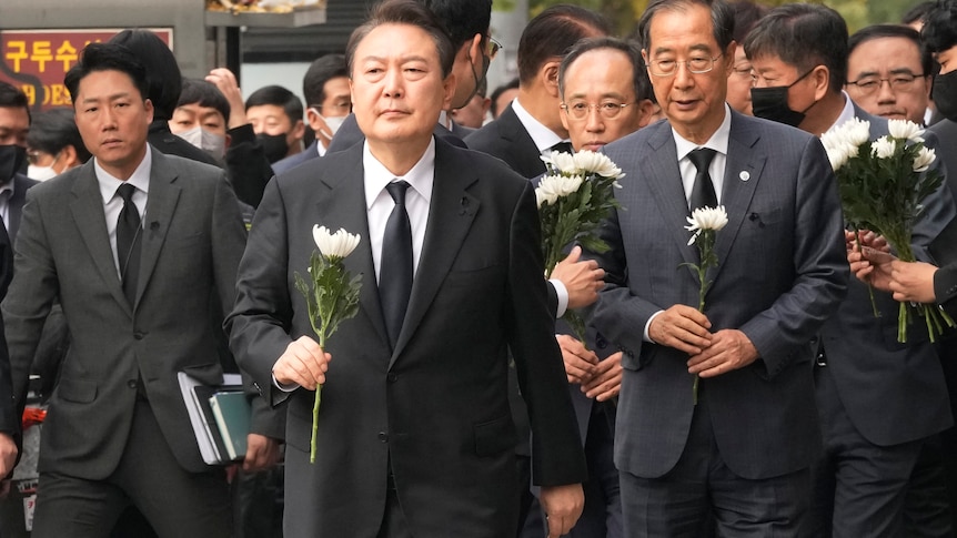 A group of men in suits all carrying white flowers