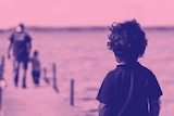 Young boy looks on at a father and a child on a jetty for a story about the effects of not being shown kindness when young.
