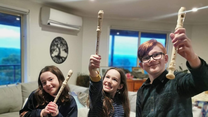 Three children holding recorders triumphantly in the air.