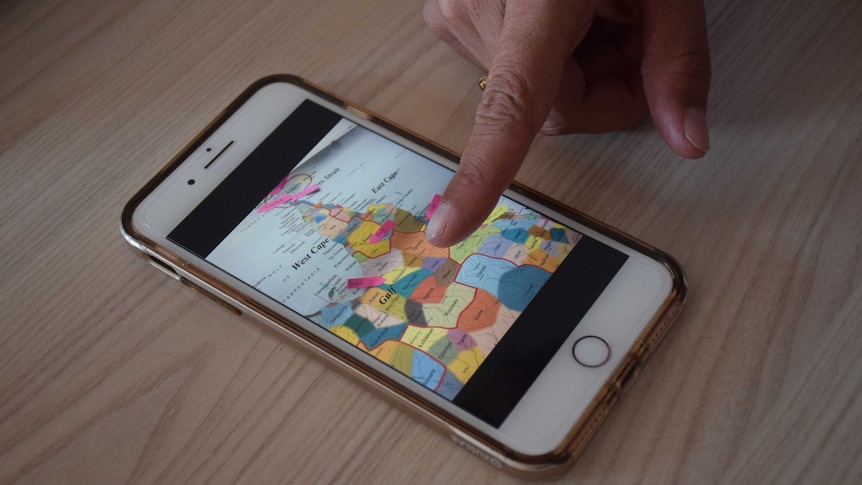 A close up of a finger pointing at a smart phone which ahs a photo of a map divided by tribe names