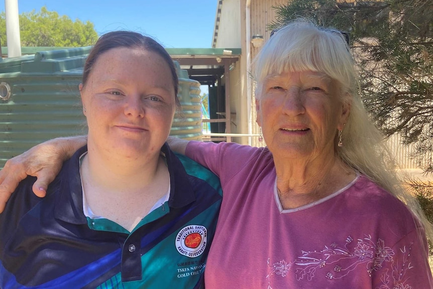 A younger woman and an older woman stand outside on a hot day, smiling at the camera.