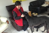 Janet Flan sitting and patting a dark-coloured greyhound.