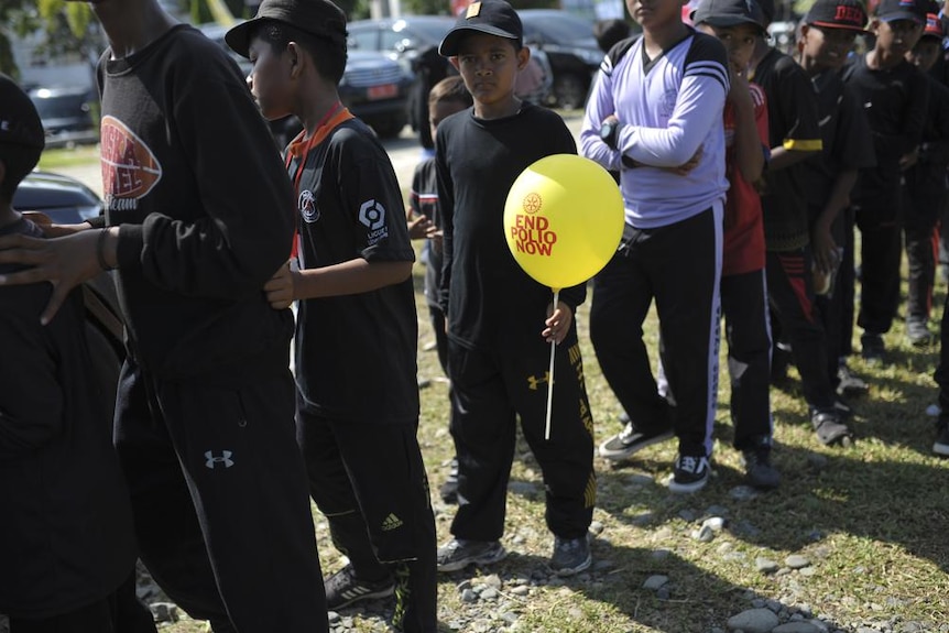 Children lining up for polio vaccination with one boy hold a balloon with a writing saying end polio now