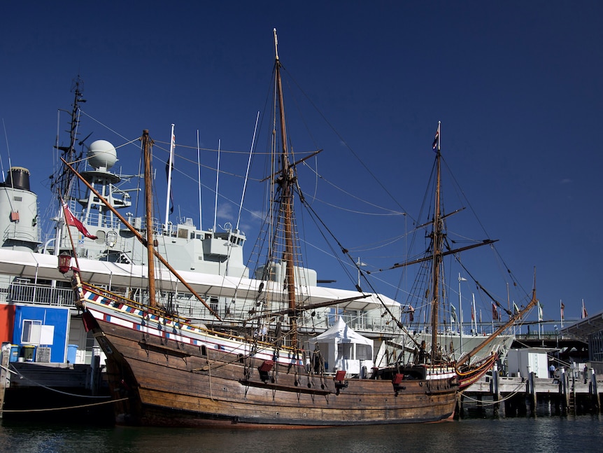 A replica tall ship moored in a harbour marina.