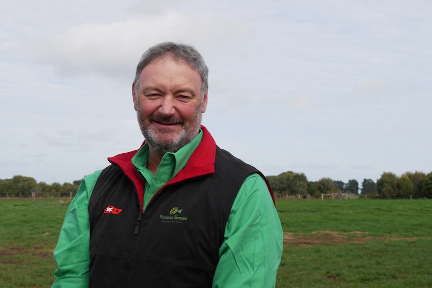 A smiling farmer with a grey beard and short hair standing in a paddock.