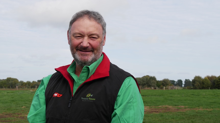 A smiling farmer with a grey beard and short hair standing in a paddock.