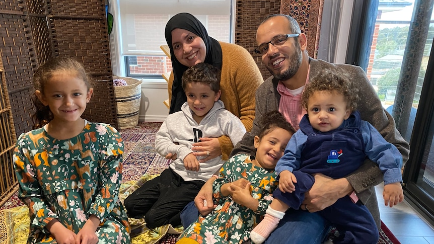 A Muslin family - two parents and three children - sitting on the ground at home. 