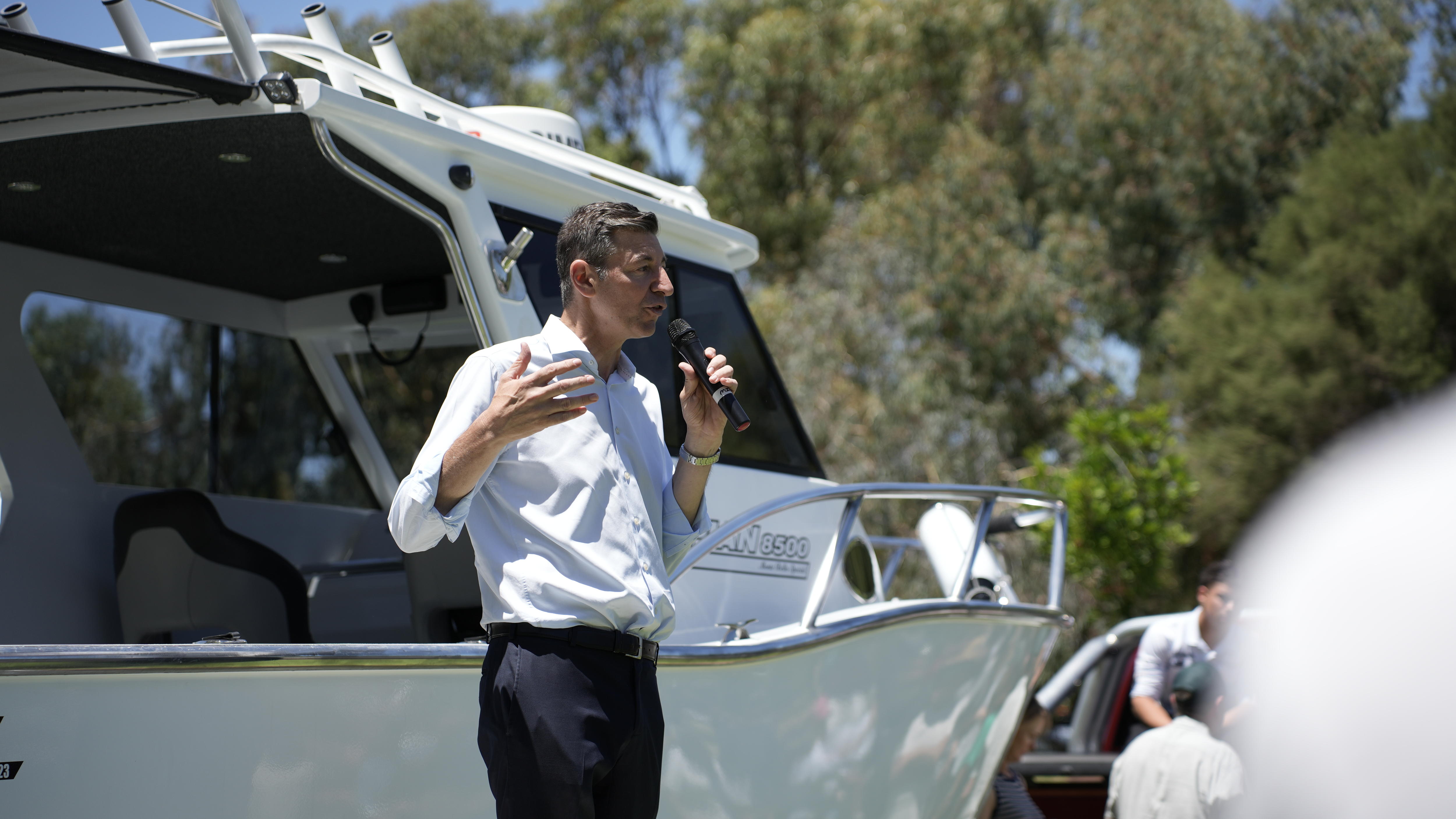El líder de la oposición de WA, Basil Zempilas, habla mientras está parado frente a un barco. 