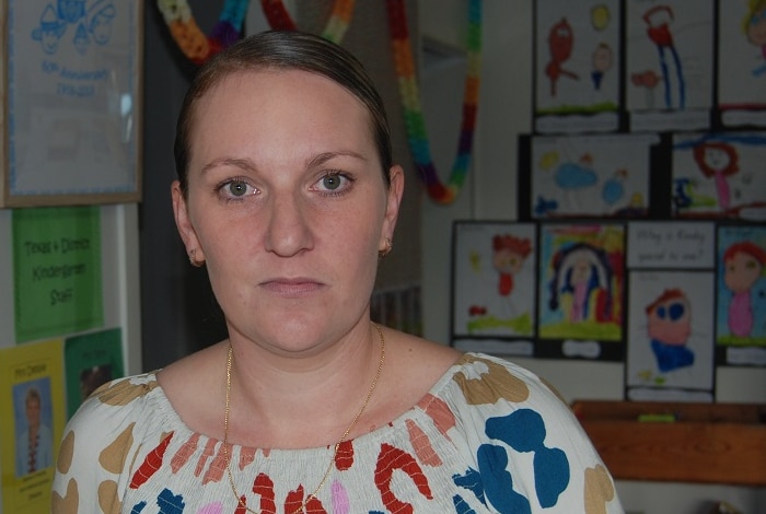 A woman stand before a wall filled with children's drawings on individual pieces of paper.