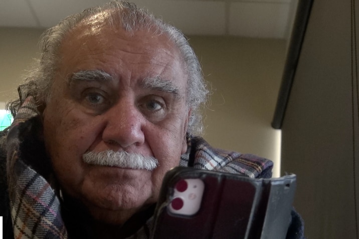 An Aboriginal man with white hair looks at the camera