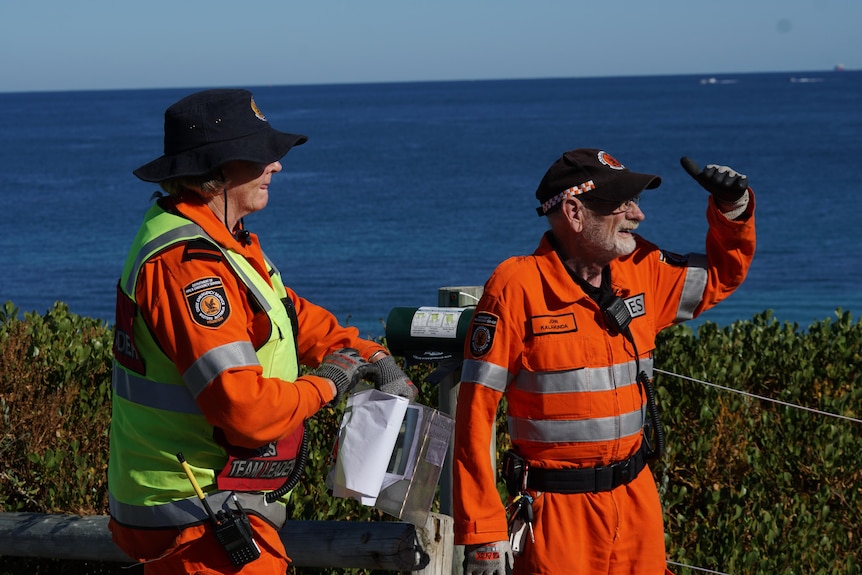 Two SES volunteers standing in scrub-covered dunes and looking into the distance.