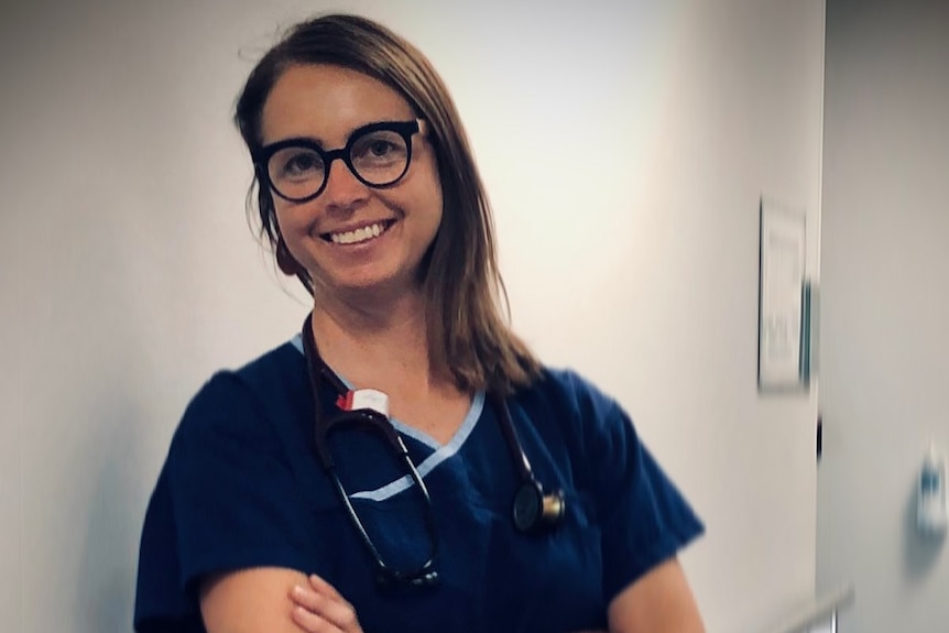 A doctor leans against a hallway in scrubs