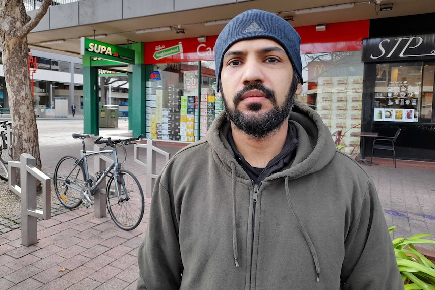 A man in a beanie stands outside a store.