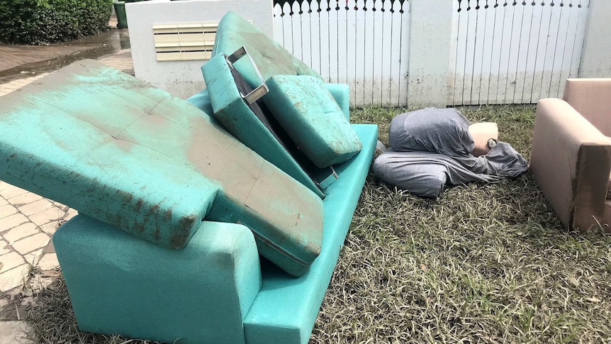 A muddy couch sits discarded outside a townhouse.