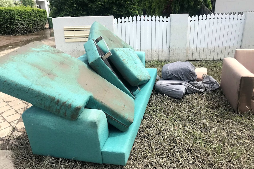 A muddy couch sits discarded outside a townhouse.