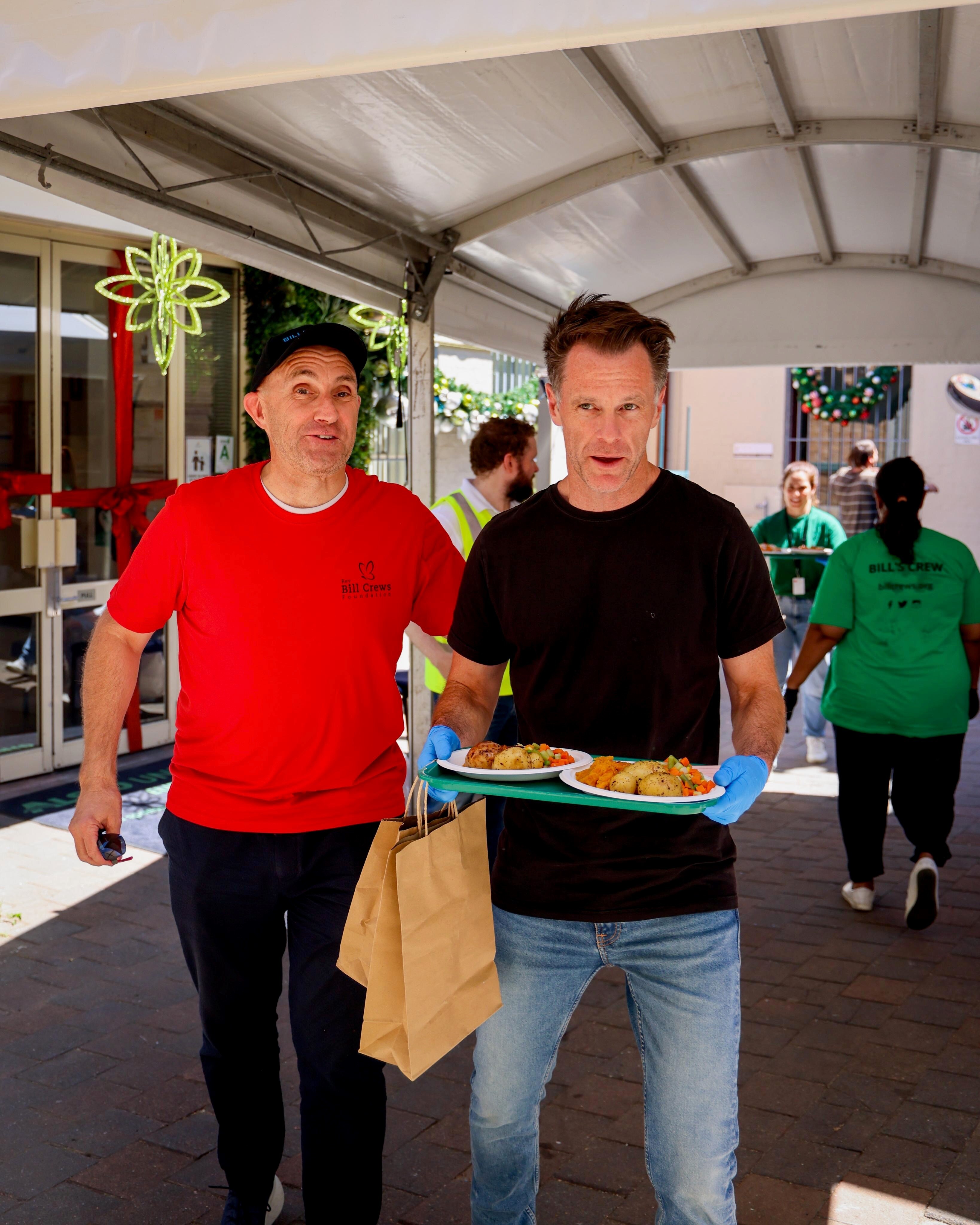 NSW Premier Chris Minns carries a tray of christmas day lunch as he walks with a volunteer helping out at a charity