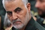 General Qassem Soleimani in military uniform with grey hair and dark eyebrows glances from crowd of military men.