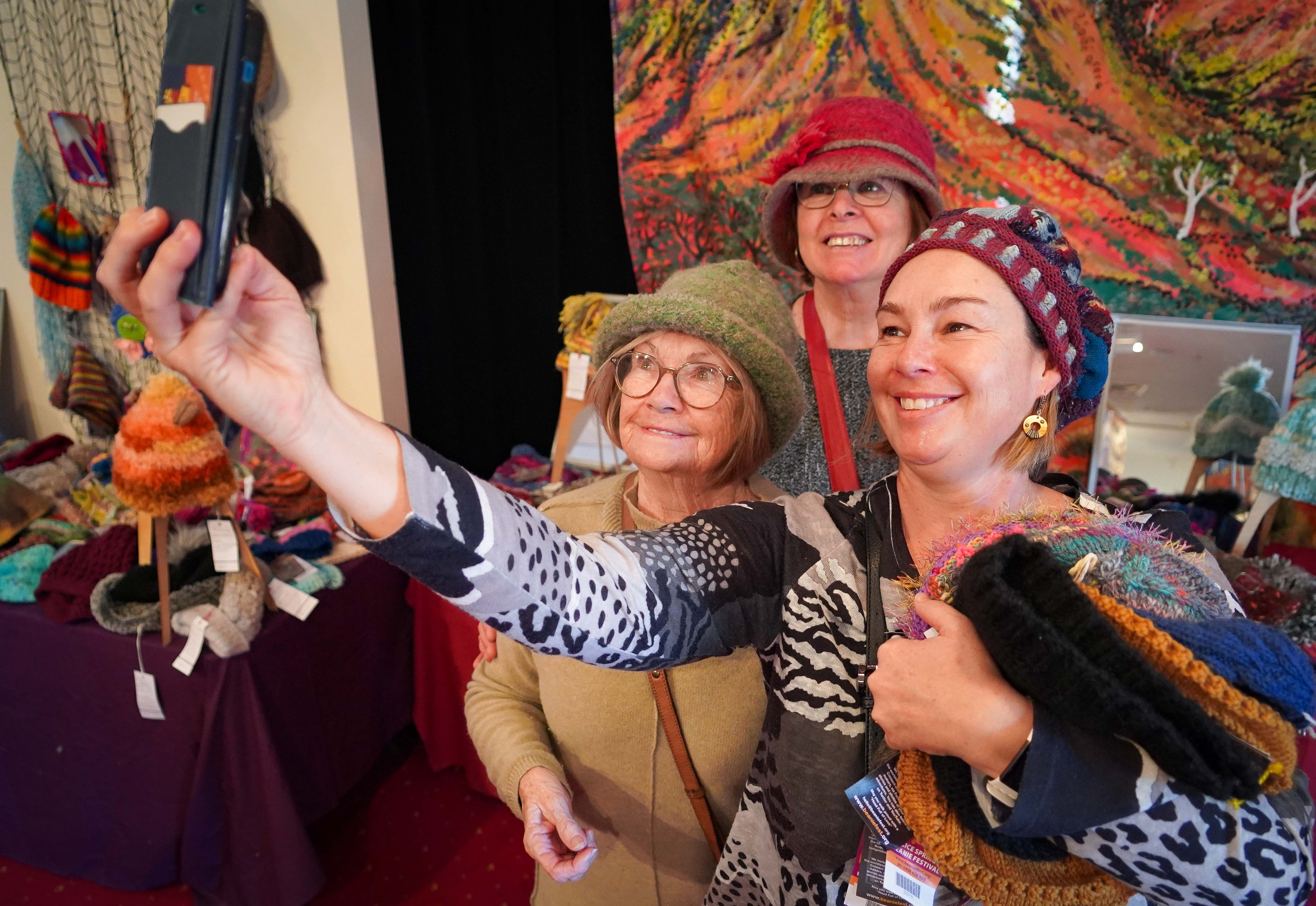 A group of women wearing colourful knit beanies, smiling as they take a photo together.