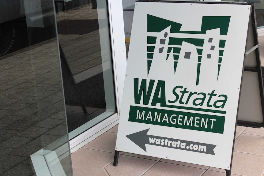 An A-frame sign for WA Strata Management on the ground outside a glass door.