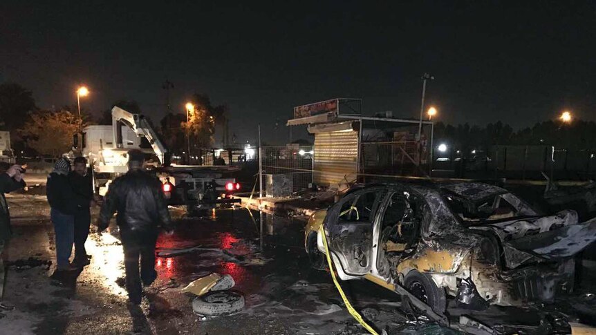 Iraqi officials observe burnt out cars at the site of a suicide attack in Baghdad.